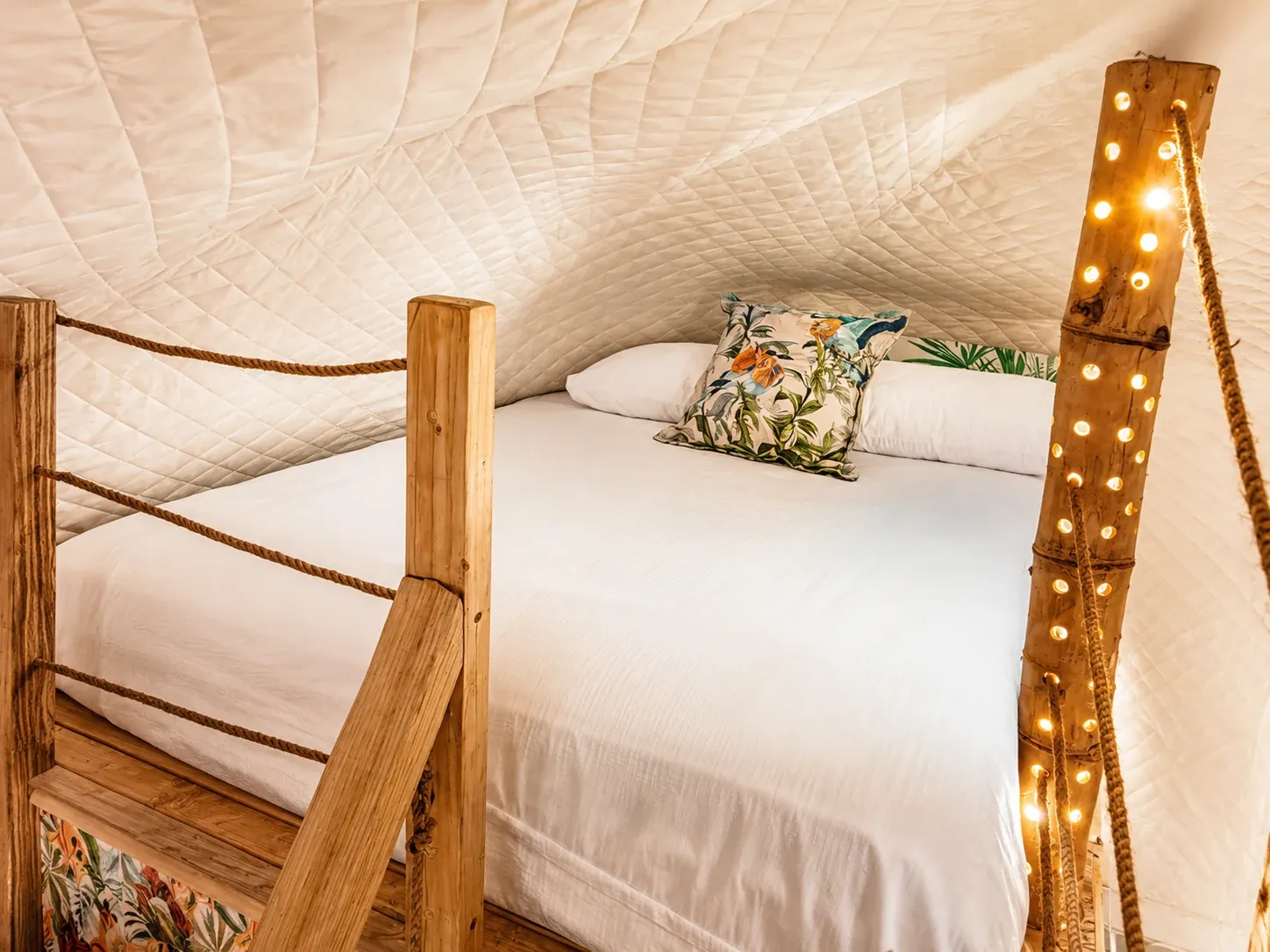 Loft bed inside a glamping dome with a wooden balustrade and fairy lights